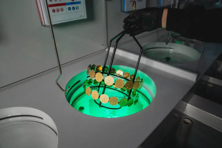 Cadrans de montre Montremo disposés sur un support métallique, plongés dans un bain lumineux pour l’adoucissage et le polissage de leur surface