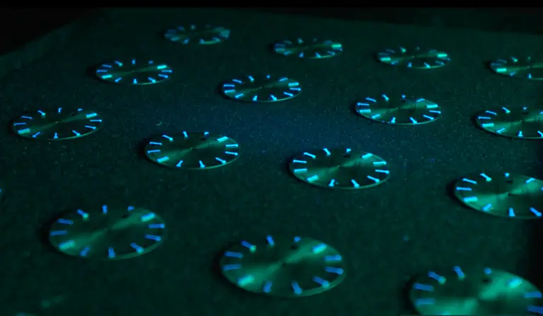 Série de cadrans de montre posés sur un plateau noir, dont les index enduits de Super‑Luminova émettent une lueur bleu‑verte dans le noir