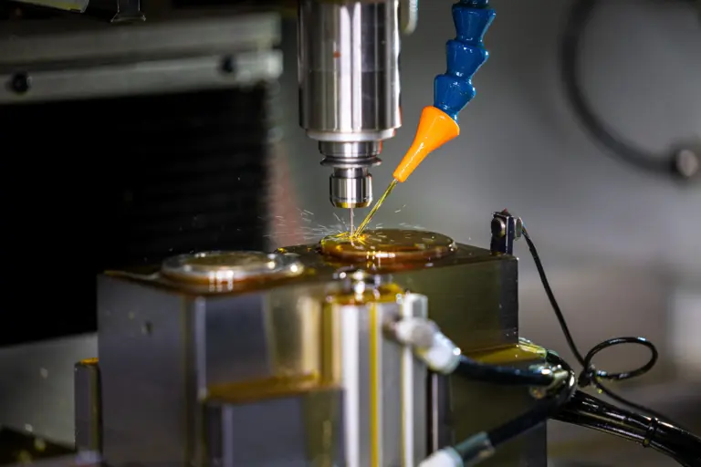 Gros plan sur une machine-outil qui usine un cadran de montre, perçant avec précision les trous d’aiguilles tandis qu’un jet de lubrifiant accompagne la coupe